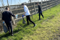 Uczniowie zbierają śmieci w tle płot