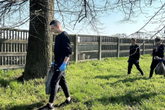 Uczniowie z czarnymi workami w rękach idą, w tle płot, drzewa