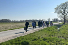 Grupa osób idzie drogą w tle pole, niebo