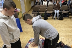 Dwóch uczniów klęczy przy fantomie, jeden z nich robi uciski mostka