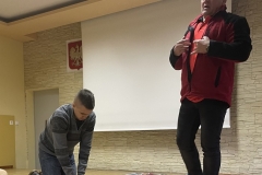 Ratownik medyczny stoi, uczeń klęczy przy fantomie