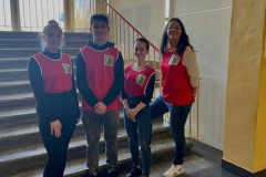 Nauczycielka i uczniowie w czerwonych koszulkach stoją przy schodach