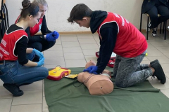 Uczeń klęczy przy fantomie, obok kucają dwie uczennice
