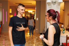 Mężczyzna z dłonią na klatce piersiowej rozmawia z kobietą, w tle inne osoby