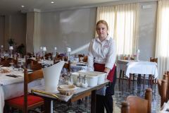 Kobieta pcha wózek na którym stoją cukiernice, pojemniki plastikowe, w tle stoliki