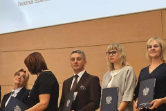 Kobiety i mężczyżni z dyplomami w ręku stoją, w tle imiona i nazwiska osób