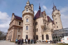 Grupa osób stoi koło budynku z wieżami