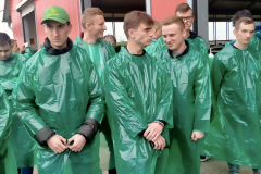 Uczniowie ubrani w fartuchy z zielonej folii stoją przed budynkiem