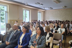 Mężczyźni i kobiety siedzą na krzesłach, w tle okna