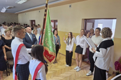 Młodzież w strojach galowych stoi przy sztandarze szkoły