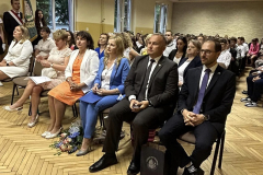 Uczestnicy akademii siedzą na krzesłach, w tle otwarte okna