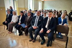 Grupa osób siedzi na krzesłach w tle okna