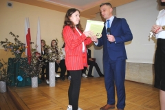 Dyrektor szkoły i wychowawczyni wręczają nagrodę i świadectwo uczennicy, w tle ściana