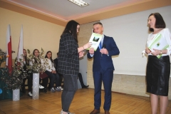 Dyrektor szkoły i wychowawczyni wręczają świadectwo uczennicy, w tle ściana