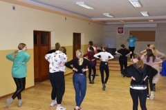 Uczniowie rozstawieni po sali ćwiczą kroki tańca