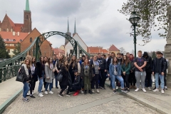 Uczniowie stoją. W tle Most Tumski, stare miasto Wrocławia.